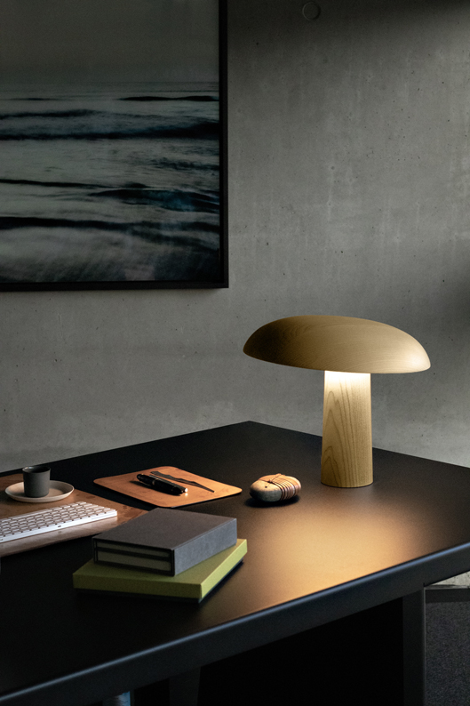 Leuchte Forma von Classicon in hellem Eschenholz auf einem schwarzen Schreibtisch.