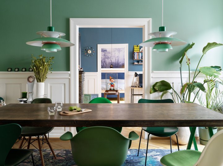 Altbau-Wohnzimmer mit grün gestrichenen Wänden und schwarzem rechteckigen Esstisch mit verschiedenen Designerstühlen ebenfalls in grün.