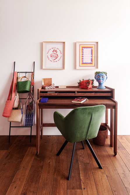 Blick auf Arbeitstisch aus dunklem Holz vor weiser Wand mit zwei kleinen Bildern und Stuhl aus dunkel grünem Samt.