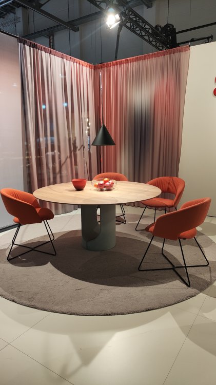 Ein Foto eines runden Hellbrauen Tisches, der von roten Stühlen umgeben ist.