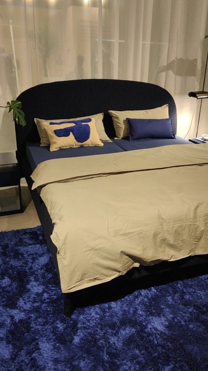 Ein Foto eines Bettes mit beigen Bouvet, welches auf einem blauen Teppich steht.