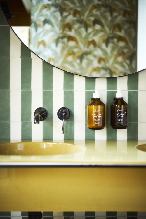 Chez Fritz – Waschraum mit grün-weissen Fliesen und gelbem Lavabo im Retro-Design.