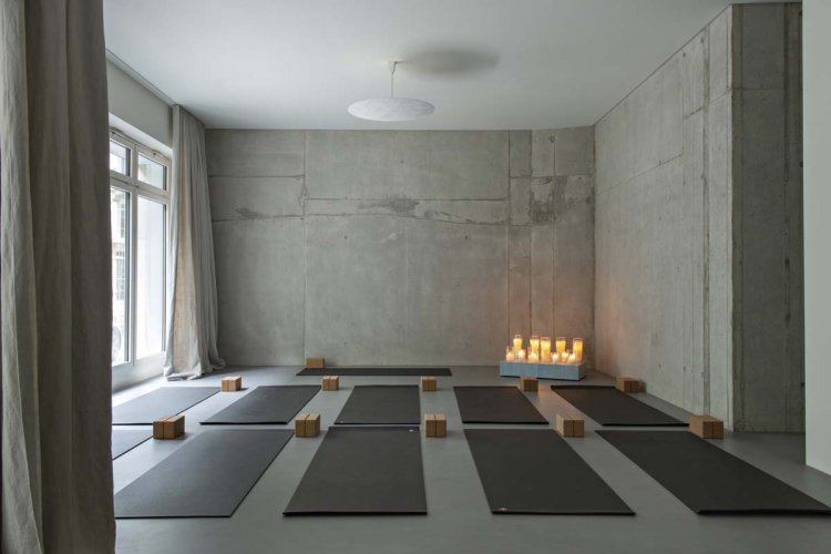 Minimalistischer Yogaraum mit Betonwänden, Kerzenlicht und aufgereihten Matten in Zürich.