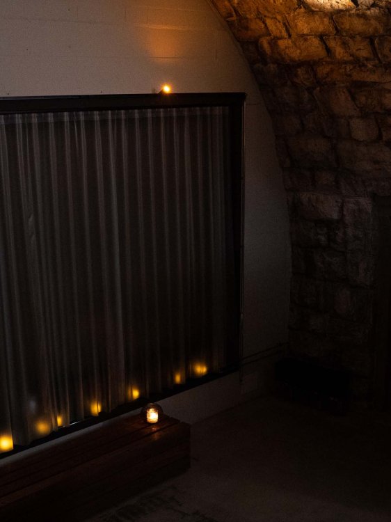 Kerzenlicht in einem Raum mit Steinwänden und Vorhängen schafft eine ruhige, meditative Stimmung.