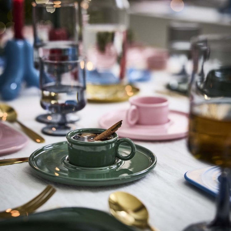 Grüne Porzellantasse mit Glögg und Zimtstange auf grosser Untertasse, Teil der IKEA x Gustaf Westman Kollektion.