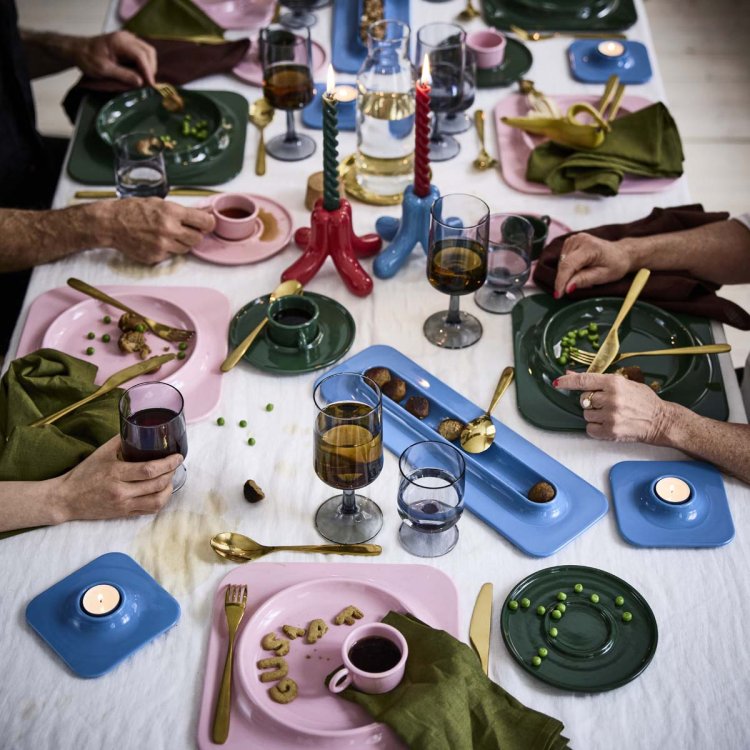 Festlich gedeckter Tisch mit buntem Geschirr und Kerzenhaltern aus der IKEA x Gustaf Westman Kollektion, Menschen sitzen zusammen und essen.