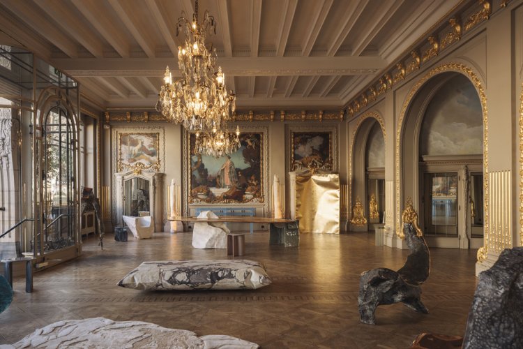 Prunkvoller Galerieraum in Brüssel mit Stuckdecken, Kronleuchtern und historischen Wandmalereien; im Vordergrund eine grosse Marmorkissen-Skulptur, im rechten Bereich ein vergoldeter Raumteiler sowie weitere zeitgenössische Skulpturen.