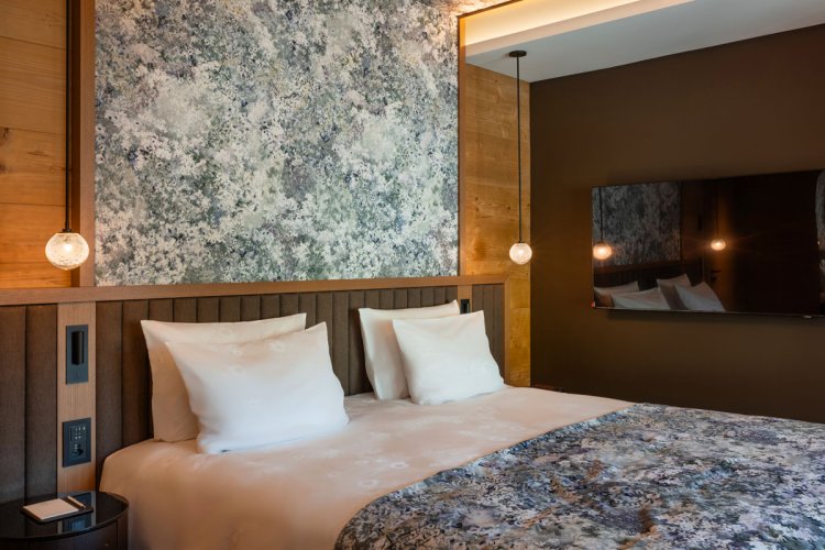 Modernes Hotelzimmer im Huus Quell mit Doppelbett, gemusterter Wand, Holzverkleidung und warmem Licht.