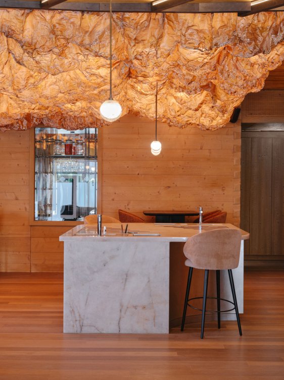 Barbereich im Huus Quell mit Marmortresen, Holzverkleidung und einer grossen, wolkenartigen Lichtinstallation über der Theke.