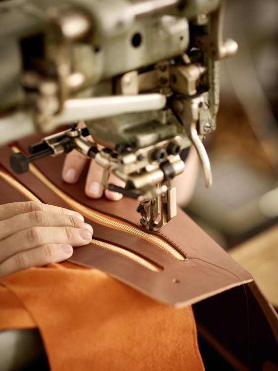 Nähmaschine näht einen Reissverschluss in ein Stück braunes Leder, Hände führen das Material präzise.