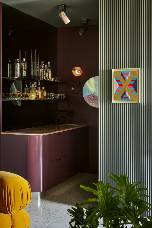 Eine etwas dunkle Nische mit einer violetten Bar. Angeschnitten im Vordergrund ein ockerfarbenes Sofa.