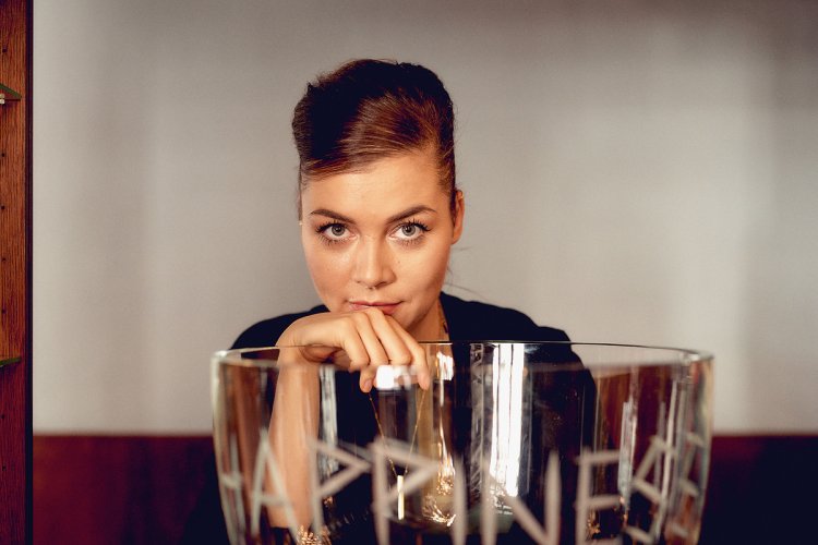 Junge Frau sitzt hinter einem Glas mit der Aufschrift Happiness