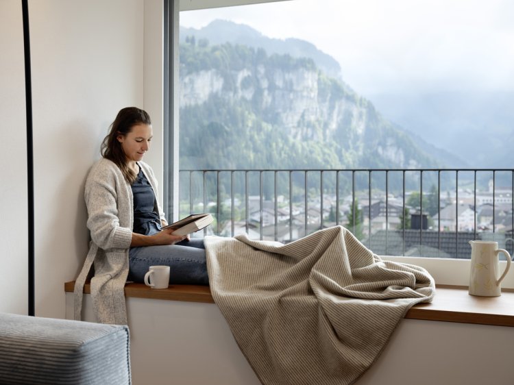 Wendy Holdener sitzt auf einer breiten Fensterbank und liest ein Buch.