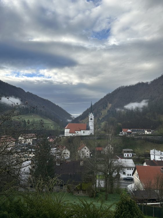 Blick auf eine Kirche, die auf einem Hügel steht. Darüber ein verhangener Wolkenhimmel.