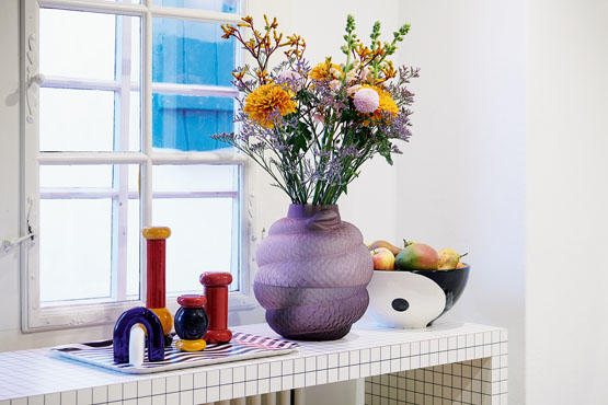 Eine Vase mit Blumen in lila steht auf einem Sideboard.