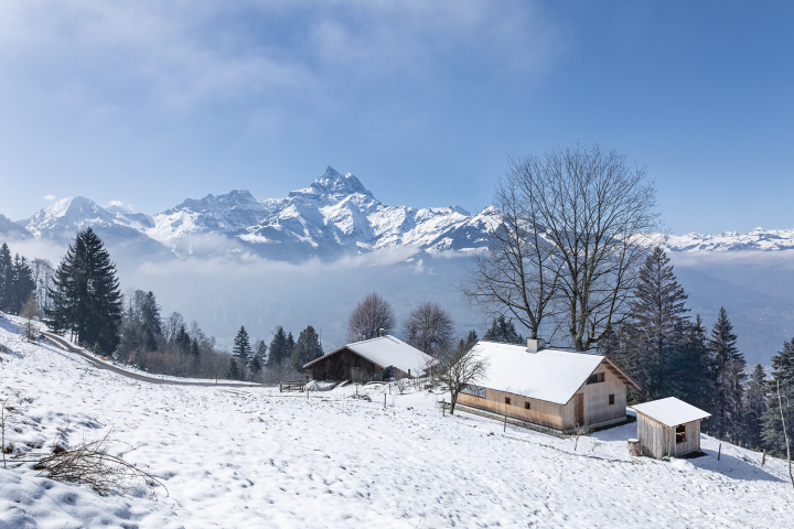 Schlichtes Holzhaus in einer Schnee bedeckten Landschaft mit Blick auf die Walliser Bergewelt