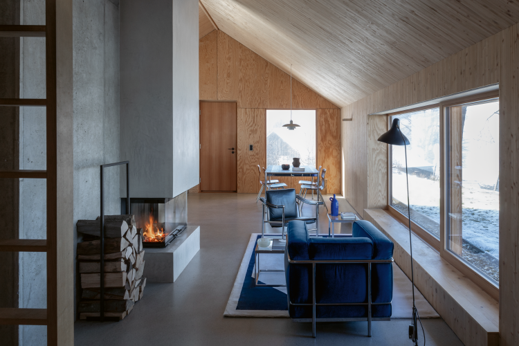 Wohnraum mit Holz ausgefacht mit Feuerstelle aus Beton. Ein blauer Sessel von Le Corbusier und Charlotte Perriand für Cassina.