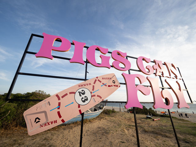 Grosse Tafel am Strand mit einem Board der neuen Sonderedition darauf befestigt und einem Schriftzug in pinker Schrift der sagt: Pigs can fly.