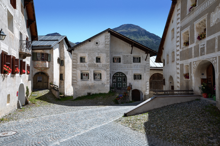 Dorfkern in Guarda mit mehreren alten Häusern. In der Mitte die Frontfassade eines Hauses aus dem 16. Jahrhundert mit alter Sgraffito-Gestaltung.
