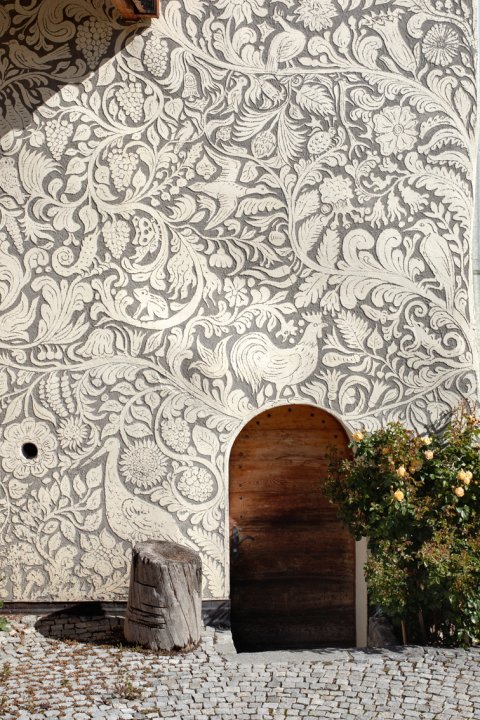 Üppig mit Pflanzen- und Tiermotiven verzierte Sgraffito-Fassade.