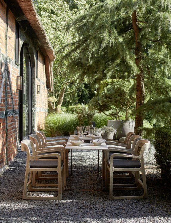 Direkt am Haus eine lange, gedeckte Holztafel mit Holzstühlen in der Mittagssonne.