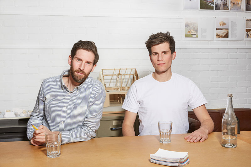 Hendrik Steinigenweg und Philipp Schaefle, die Gründer von Studio Noun, sitzen nebeneinander an einem Tisch in ihrem Büro.