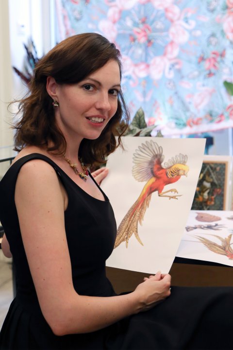 Designerin Fiona K lächelt in einem schwarzem Kleid mit selbst gemalter Zeichnung in der Hand in die Kamera