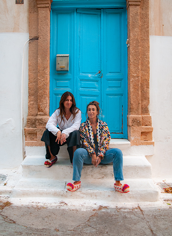 Ein Portrait von zwei Frauen die vor einer blauen Haustür sitzen.