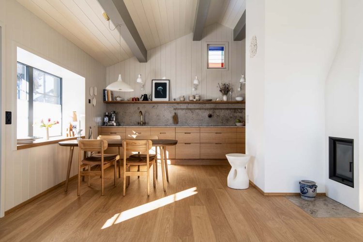 Ein Foto eines Esszimmers. Man sieht einen Holztisch mit Holzstühle, dahinter steht eine Küche.