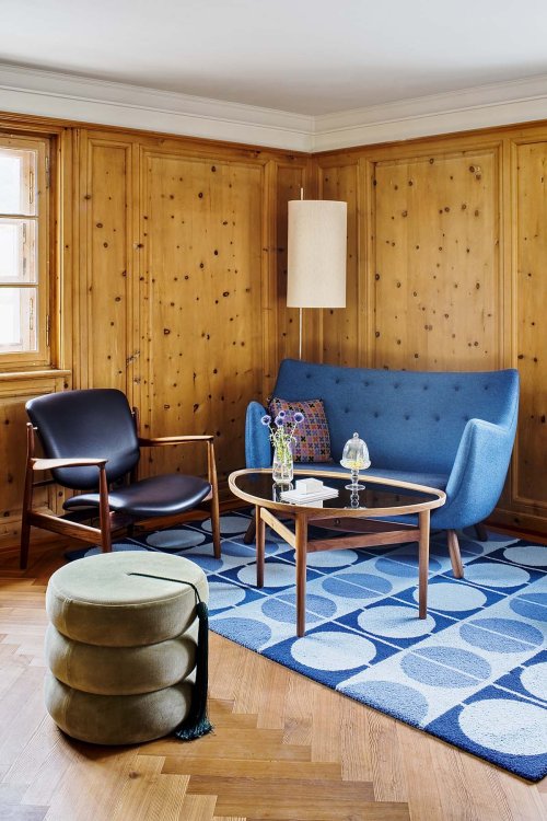 Ein Foto eines Sitzecken, in welchem ein dunkelblauer Sessel steht, eine hellblaue Couch und ein Beistelltisch. Die Möbel stehen auf einem blauen Teppich.