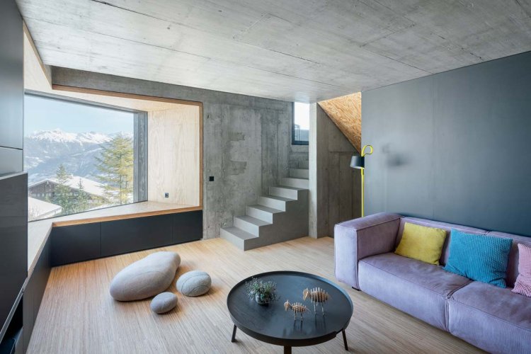 Ein Foto des Wohnraums. Zu sehen ist ein lila Sofa, vor welchem ein schwarzer Beistelltisch steht. Der Raum hat grosse Fenster und ermöglicht eins schönes Panorama.
