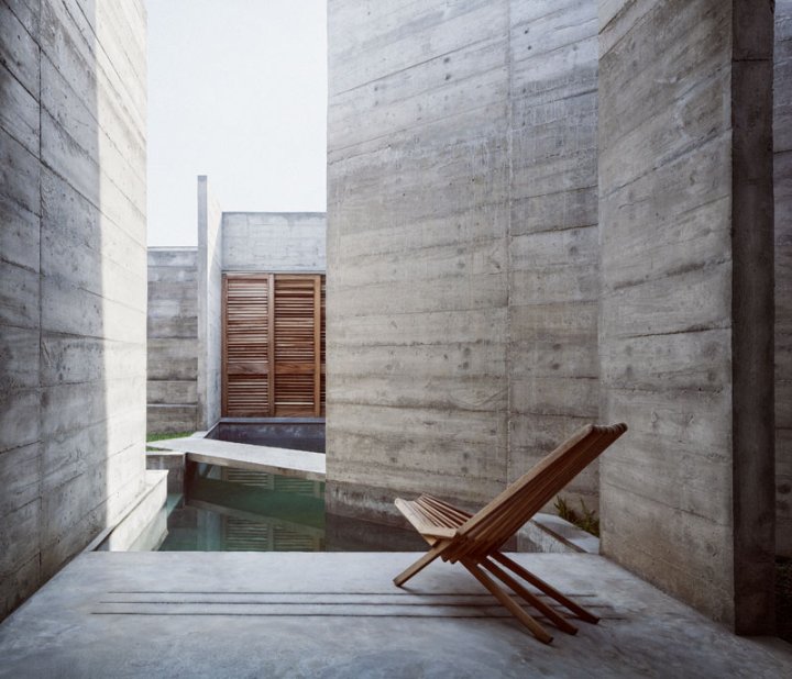 Eine Terrasse mit einem Liegestuhl aus Holz blickt an die verschlossenen Fassaden aus Beton.