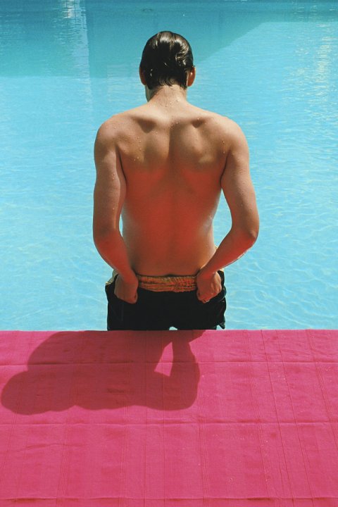 Rückenansicht eines Mannes vor einem Pool und pinken Boden.