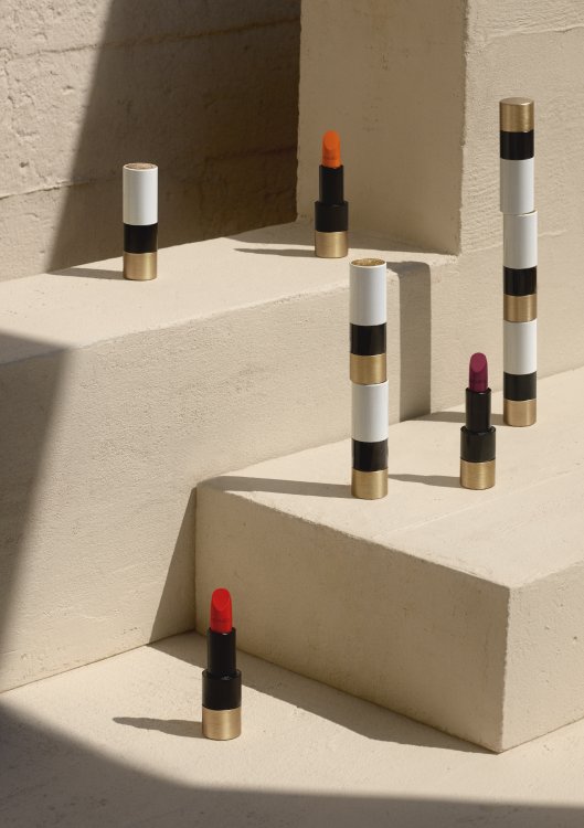 Die neu lancierten Lippenstifte aus der «Rouge Hermès»-Kollektion, drapiert auf einem sandfarbenen Stufensockel.