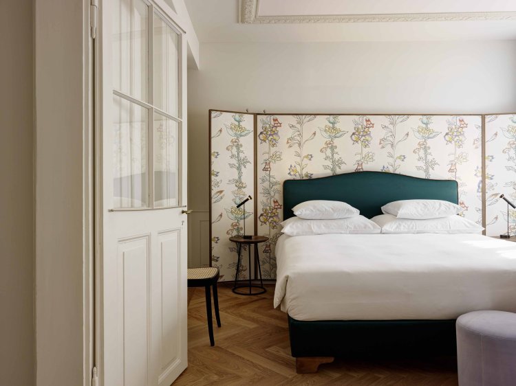 Schlafzimmer mit floral gemustertem Paravent hinter dem Bettkopfteil.