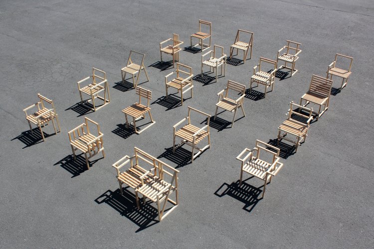 19 unterschiedliche Holzstühle aus 27mm Kantholz von Tom und Will Butterfield stehen auf einem Terrplatz in einem Quader angeordnet, leicht von oben fotografiert.