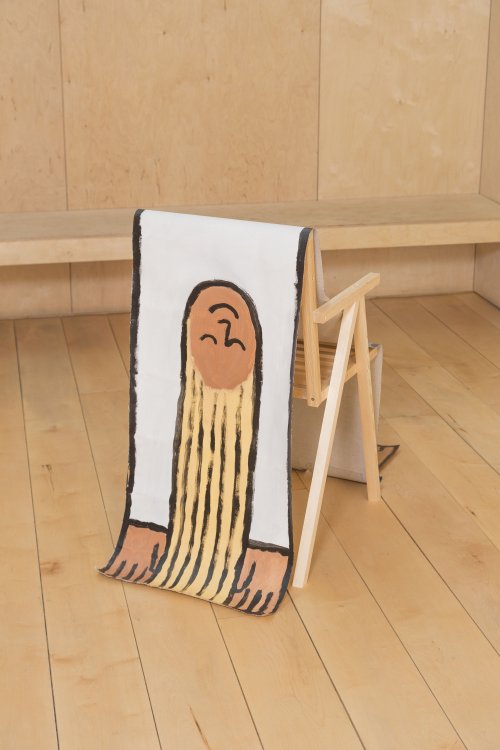 Über einem einfachen Holzstuhl hängt eine Mensch-grosse kindliche Zeichnung von Illustrator Jean Jullien einer Figur mit langen blonden Haaren und einem weissen Pullover.