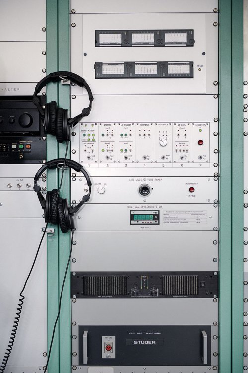 Aufnahme eines Akustikgeräts mit mehreren Knöpfen und Reglern an dem links zwei schwarze Kopfhörer aufgehängt sind.