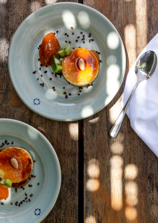 Aufsicht eines süssen Desserts mit Pudding und orangen Früchten, präsentiert auf hellblauen Tellern auf einem Holztisch.
