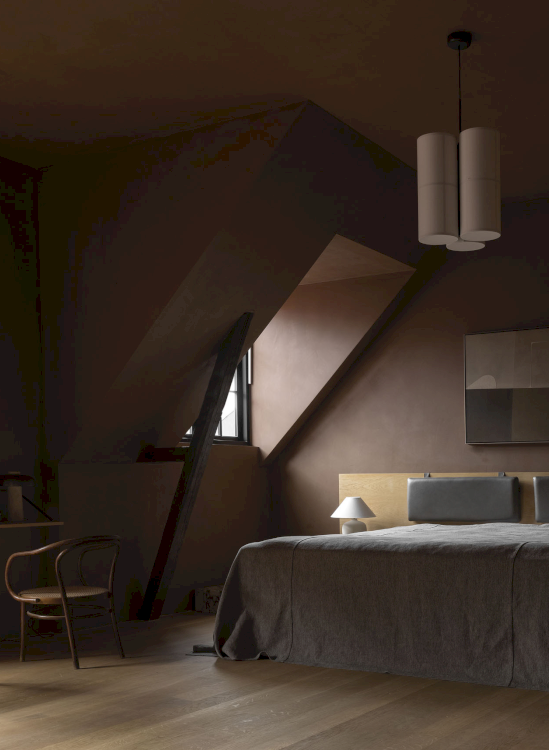 Ein dunkelrot gestrichenes Schlafzimmer mit Dachschräge in dem sich ein gemütliches Doppelbett mit grauer Bettwäsche befindet.