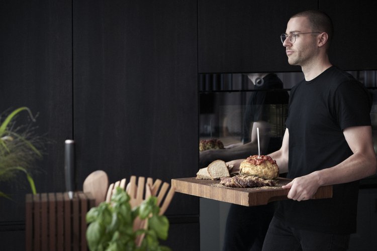 Industriedesigner Andreas Arabiano trägt die zubereiteten Köstlichkeiten auf einem Holzbrett aus der Küche.