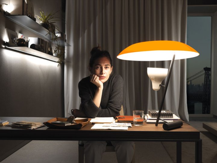 Die Protagonistin des Films, Joanna, sitzt bei Nacht an einem Schreibtisch, auf dem eine orange Tischlampe steht und blickt, den Kopf auf ihre Linke Hand gestützt, direkt in die Kamera.