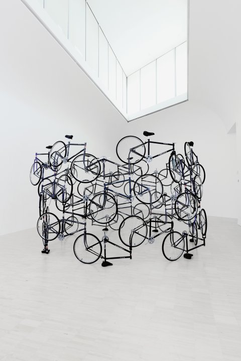 Eine Installation des Künstlers Ai Weiwei aus mehreren schwarzen Fahrrädern, die aufgetürmt und ineinander verschlungen eine Skulptur bilden.