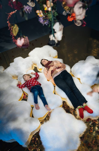 Eine Mutter und ein kleines Kind liegen unter der Installation "Verregnete Tage mit vereinzeltem Sonnenschein" von Theresa Rothe in der Kinderbiennale 2022.