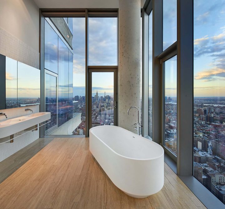 Ein modernes Badezimmer mit freistehender Badewanne vor grosser Fensterfront mit Sicht auf die New Yorker Skyline bei Sonnenaufgang.