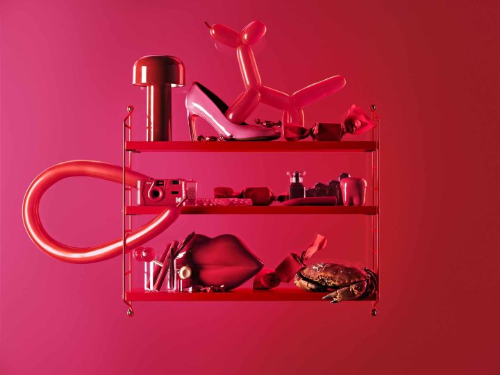 Ein rot-pinkes Wandregal mit diversen Wohnaccessoires und Gegenstände in Pinktönen vor einem ebenfalls pinken Hintergrund.