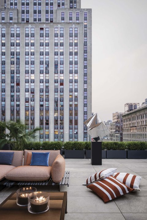 Eine Dachterrasse in New York mit Sofa und gestreiften grossen Sitzkissen, Hochhäuser im Hintergrund.