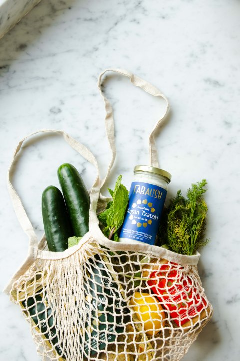 Eine geflochtene Einkaufstragetasche mit frischem Gemüse und Obst liegt auf einem Marmorhintergrund.