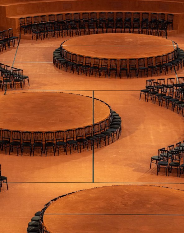 Runde, mit orangem Textil eingekleidete Podeste, um die schwarze Stühle angeordnet sind, bilden das Setting für die Lacoste-Fashionshow im Tennisstadion Roland Garros.