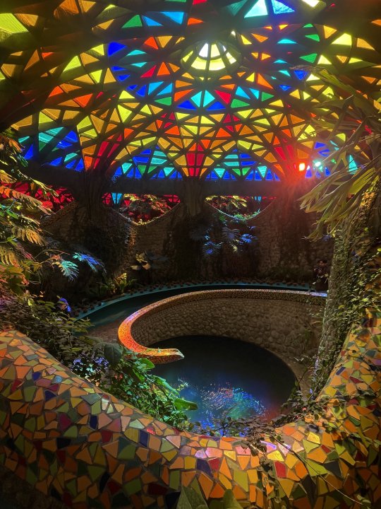 Ein mit buntem Glas ausgestattetes Kuppelhaus in dessen Mitte sich ein Wasserbecken befindet.